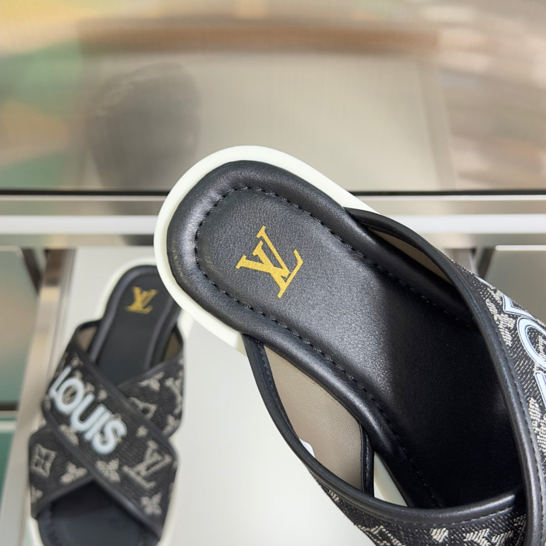Louis Vuitton slide sandal, close-up of black leather strap and gold LV emblem.