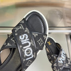 Louis Vuitton slide sandal strap close-up with white “Louis” lettering on black monogram.