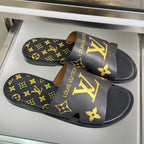 Pair of black slide sandals with gold monogram wide straps and tan trims