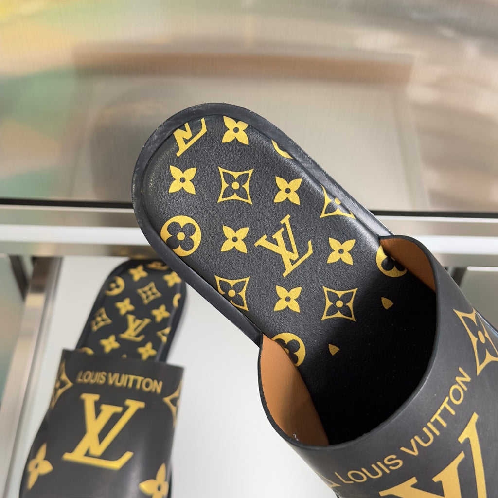 Black slide sandals with gold monogram pattern and tan interior lining
