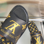 Closeup of black slide sandal strap with gold monogram flower and LV logo