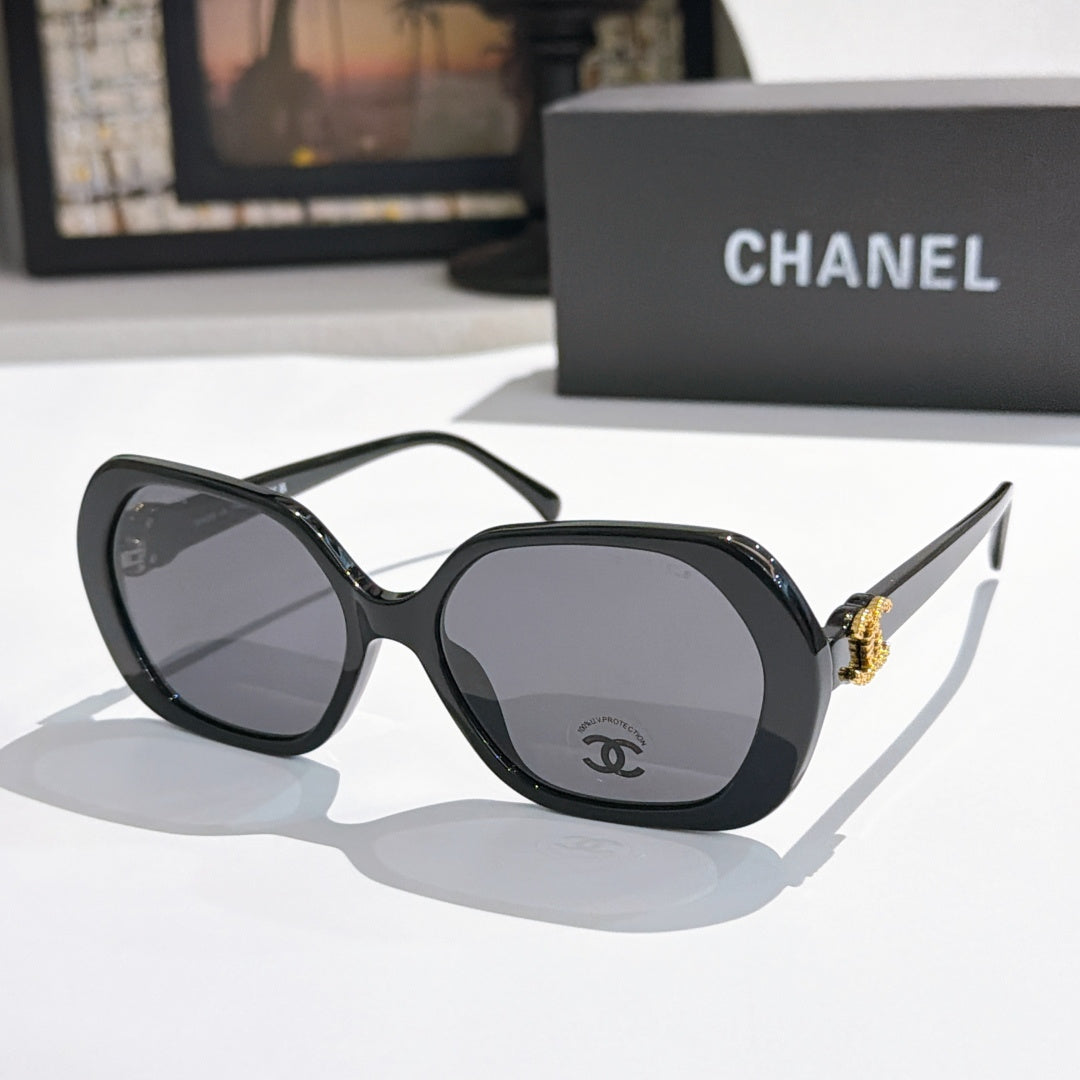 Chanel sunglasses, black frames, dark tinted lenses, gold logo detail.