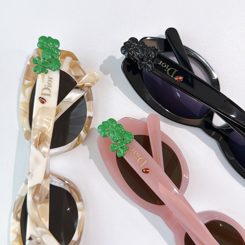 Assorted sunglasses with green floral charms, including cream, pink, and black frames