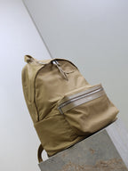 Tan nylon backpack with curved front pocket and two zip compartments with silver trim