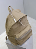 Tan nylon backpack with front-facing straps, top handle loop, and silver zip front pocket
