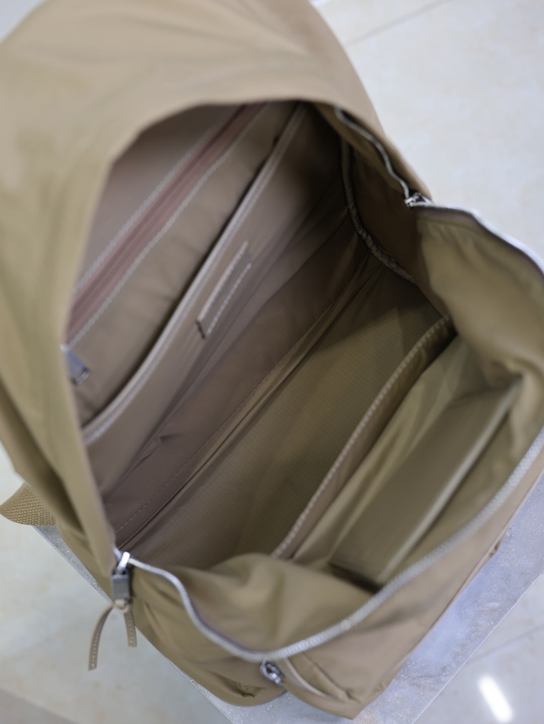 Tan backpack interior view with open top, lining pockets, and zipper closure hardware