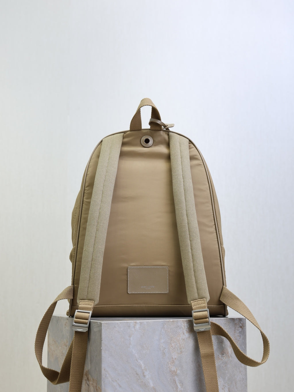 Tan nylon backpack back view with cushioned panel, straps, and small rectangular logo patch