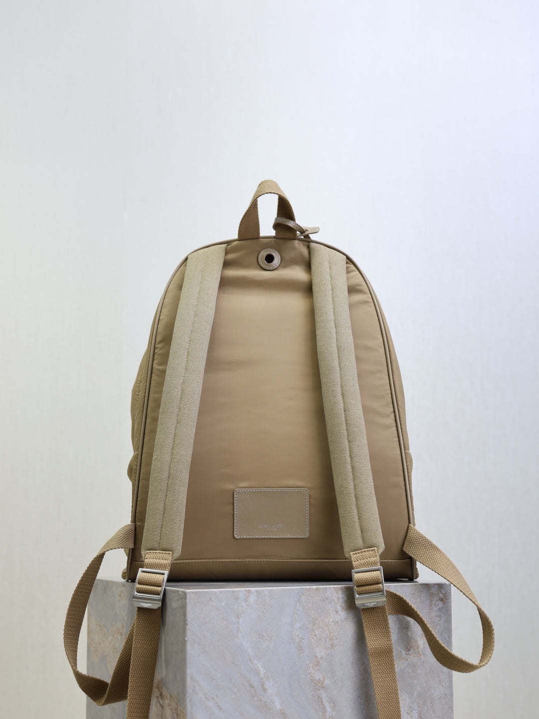 Tan nylon backpack back view with cushioned panel, straps, and small rectangular logo patch