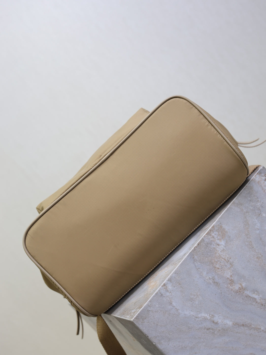 Tan nylon backpack bottom and side profile with piping edges and hanging zipper cord