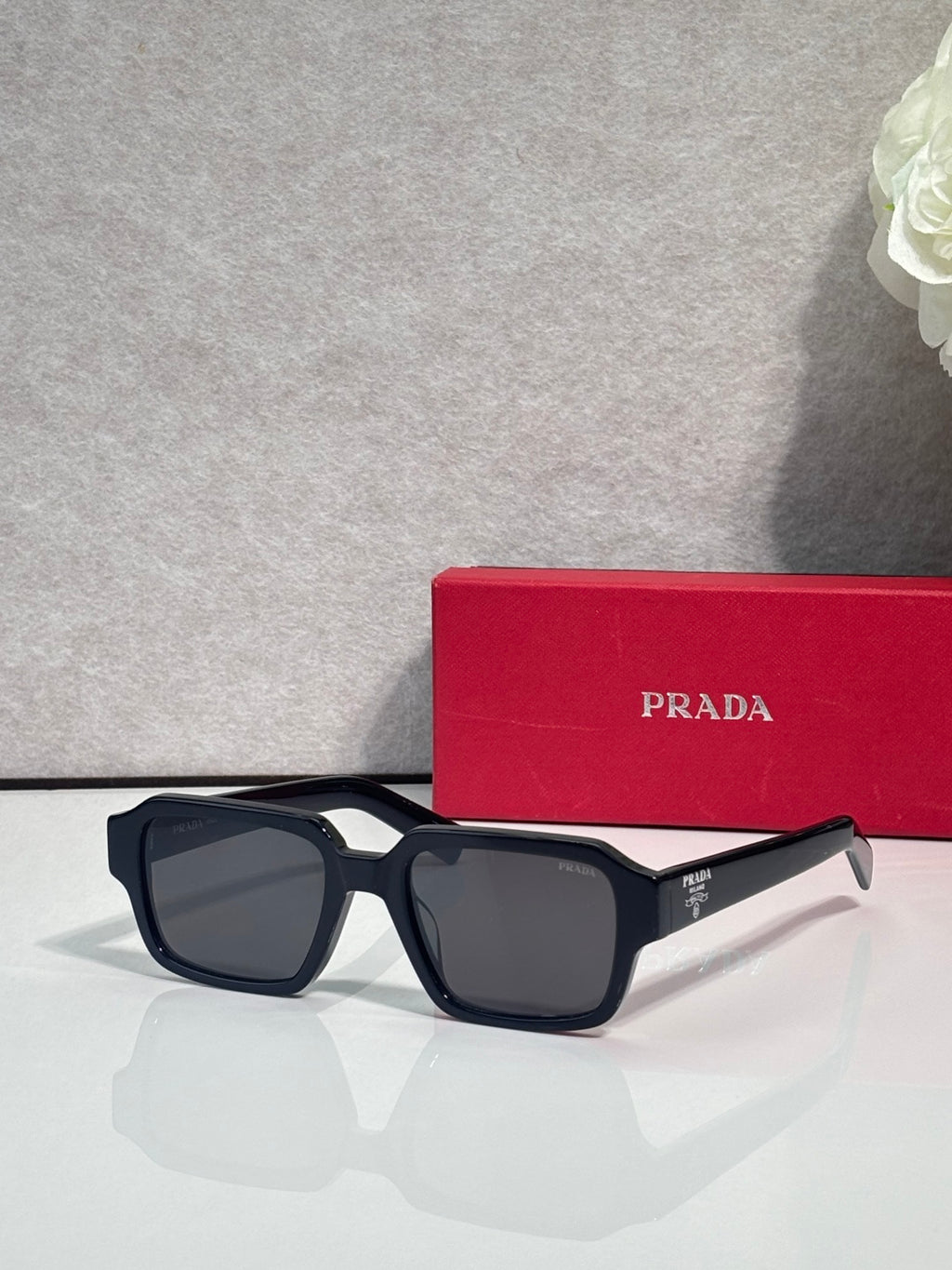 Black square sunglasses with dark lenses and silver logo detail