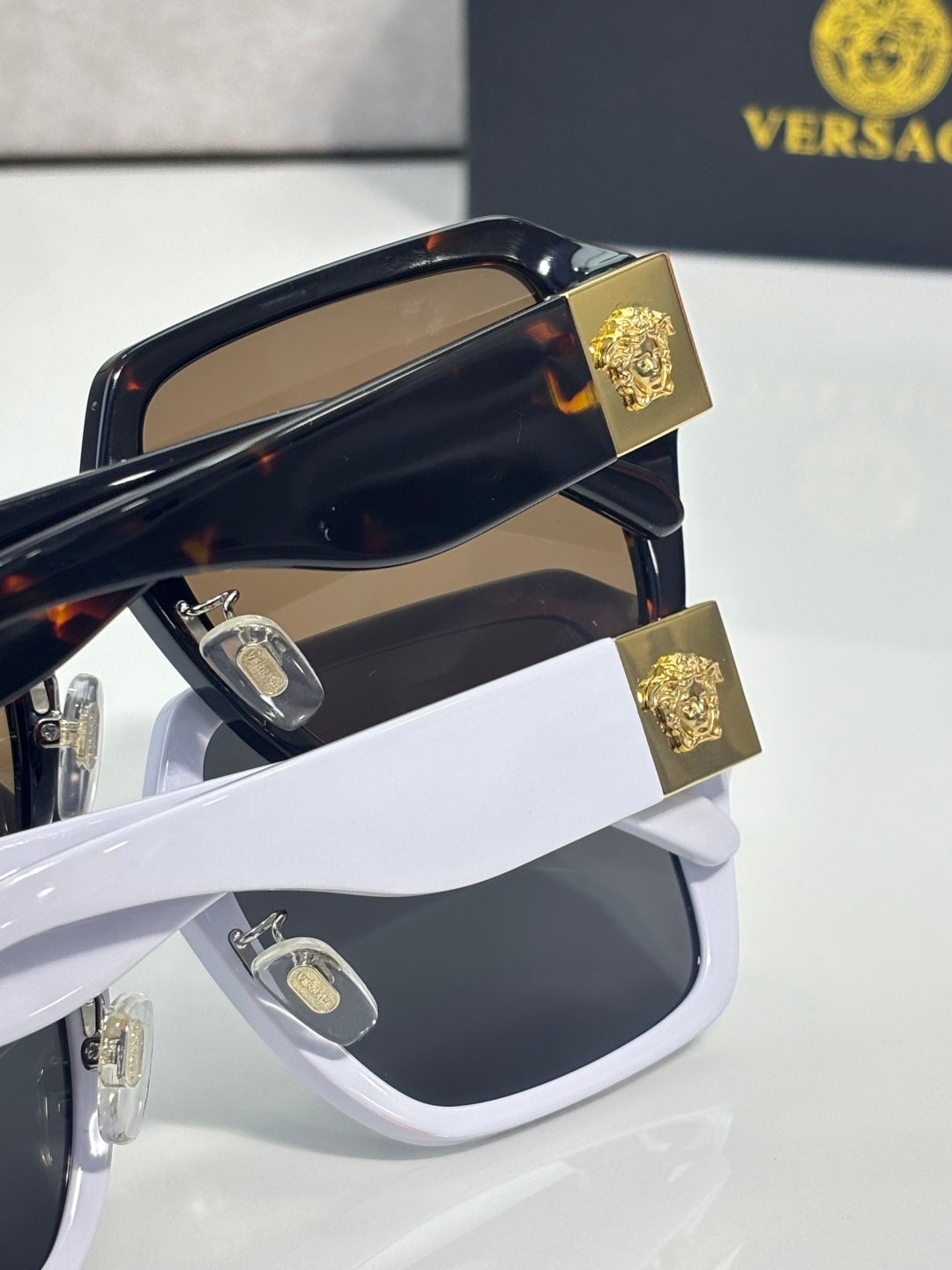Versace closeup sunglasses with gold emblem hinges, dark blue frame and brown lenses