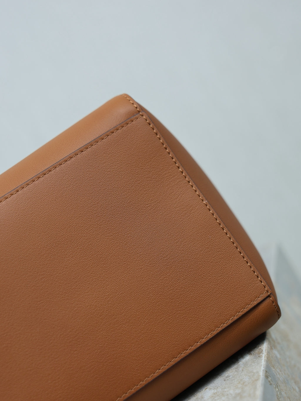 Brown leather tote bag corner with top-stitched edge and smooth grain finish