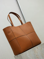 Brown leather tote bag with two top handles and cross-stitch panel seams