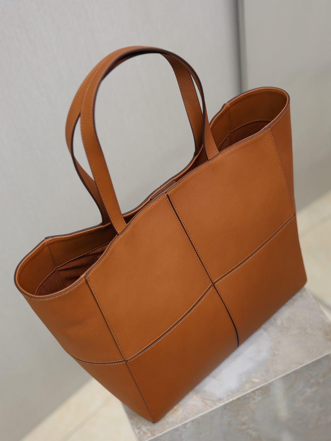 Brown leather tote bag with two handles and open top view of interior