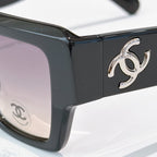 Black sunglasses close-up with silver logo on temple and dark tinted lenses
