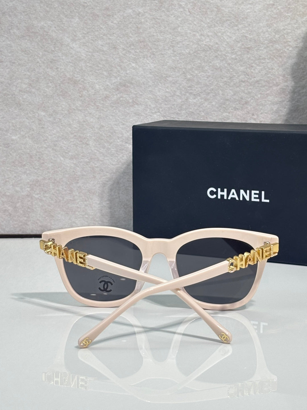 Chanel sunglasses with white frames and dark tinted lenses, gold CHANEL lettering on temples.