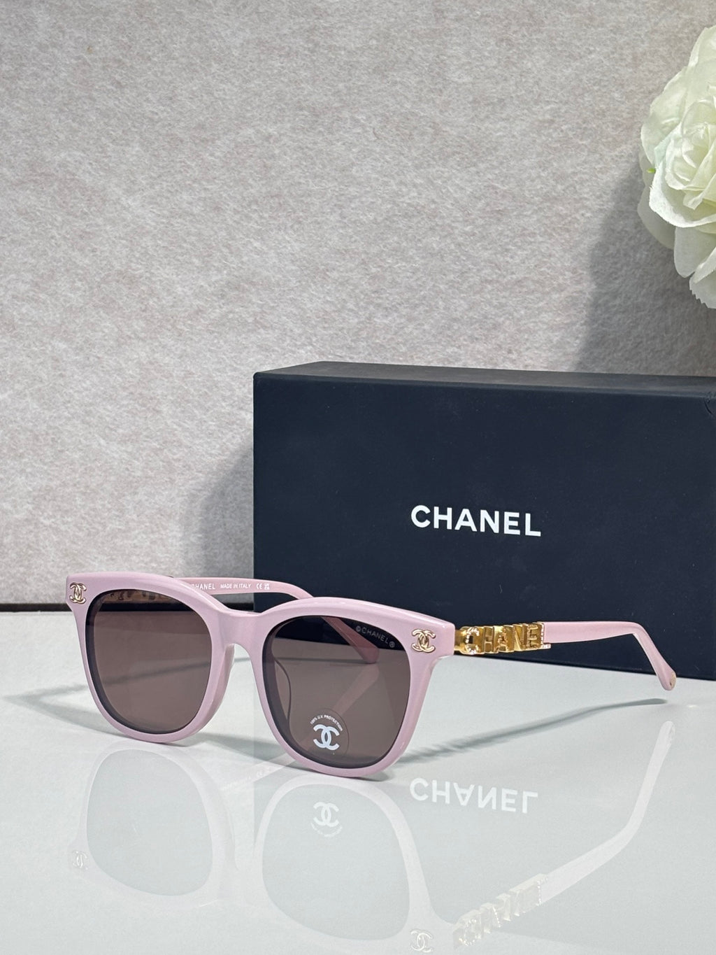 Chanel sunglasses with light pink frames and tinted lenses, gold logo accents.