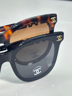 Chanel sunglasses close-up: dark tortoiseshell frames with CHANEL emblem on the temple.