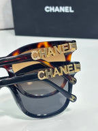 Chanel sunglasses close-up: tortoiseshell frames with gold CHANEL lettering on the temple.