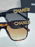 Chanel sunglasses with dark frames, gold CHANEL bar logo accents on top rim and temple