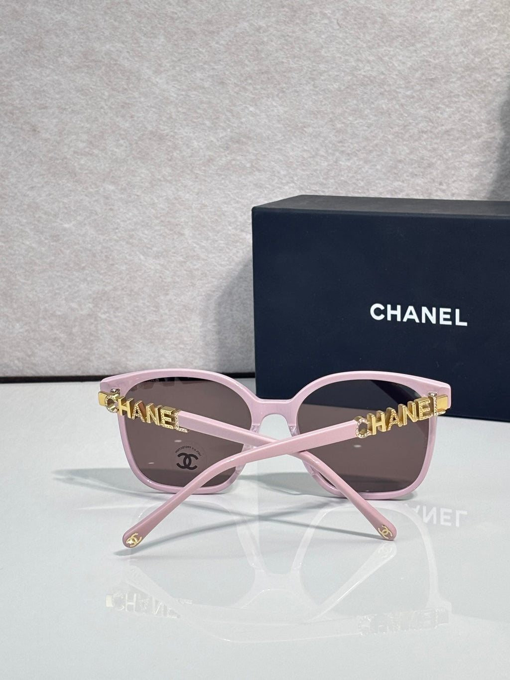 Chanel sunglasses with pink frames and brown tinted lenses, gold CHANEL logo detail on temples