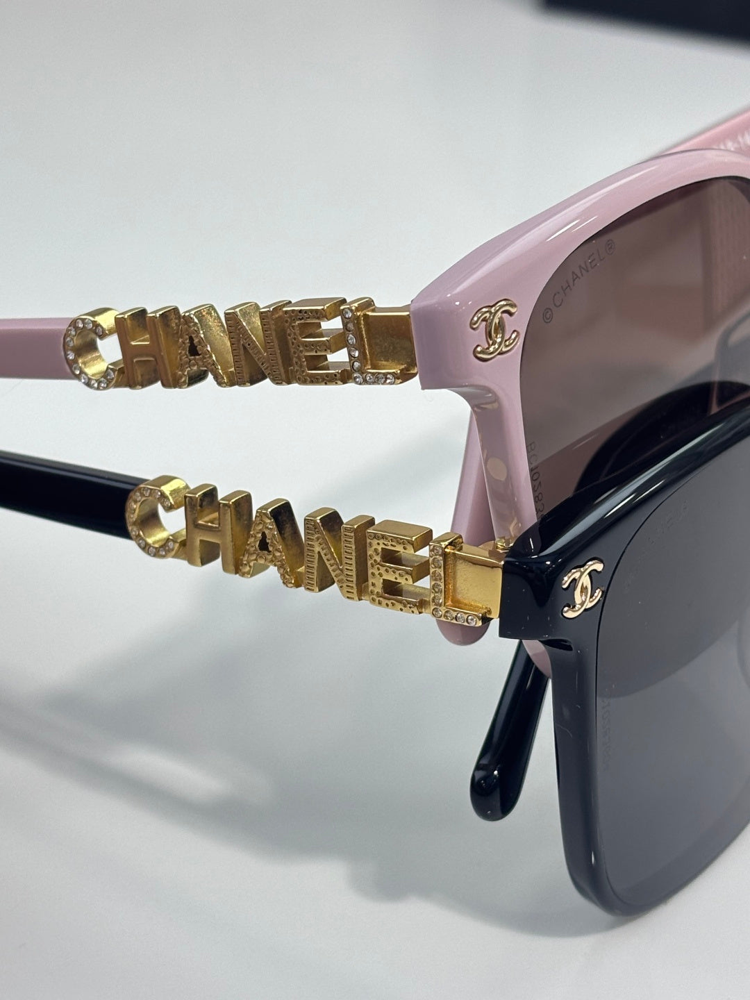 Chanel sunglasses close-up with pink frame and gold CHANEL bar logo accents on temple