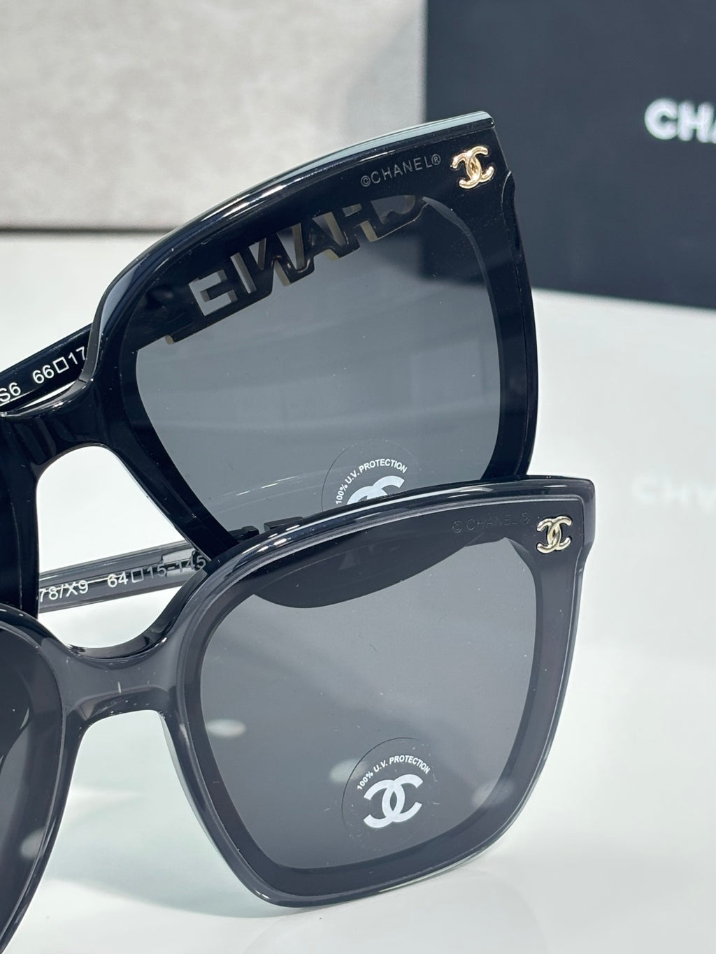 Oversized cat-eye sunglasses with dark frames and gray lenses, gold “CHANEL” accent
