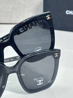 Oversized cat-eye sunglasses with dark frames and gray lenses, gold “CHANEL” accent