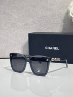 Square sunglasses with black frames and dark gray lenses, gold logo on temple arms