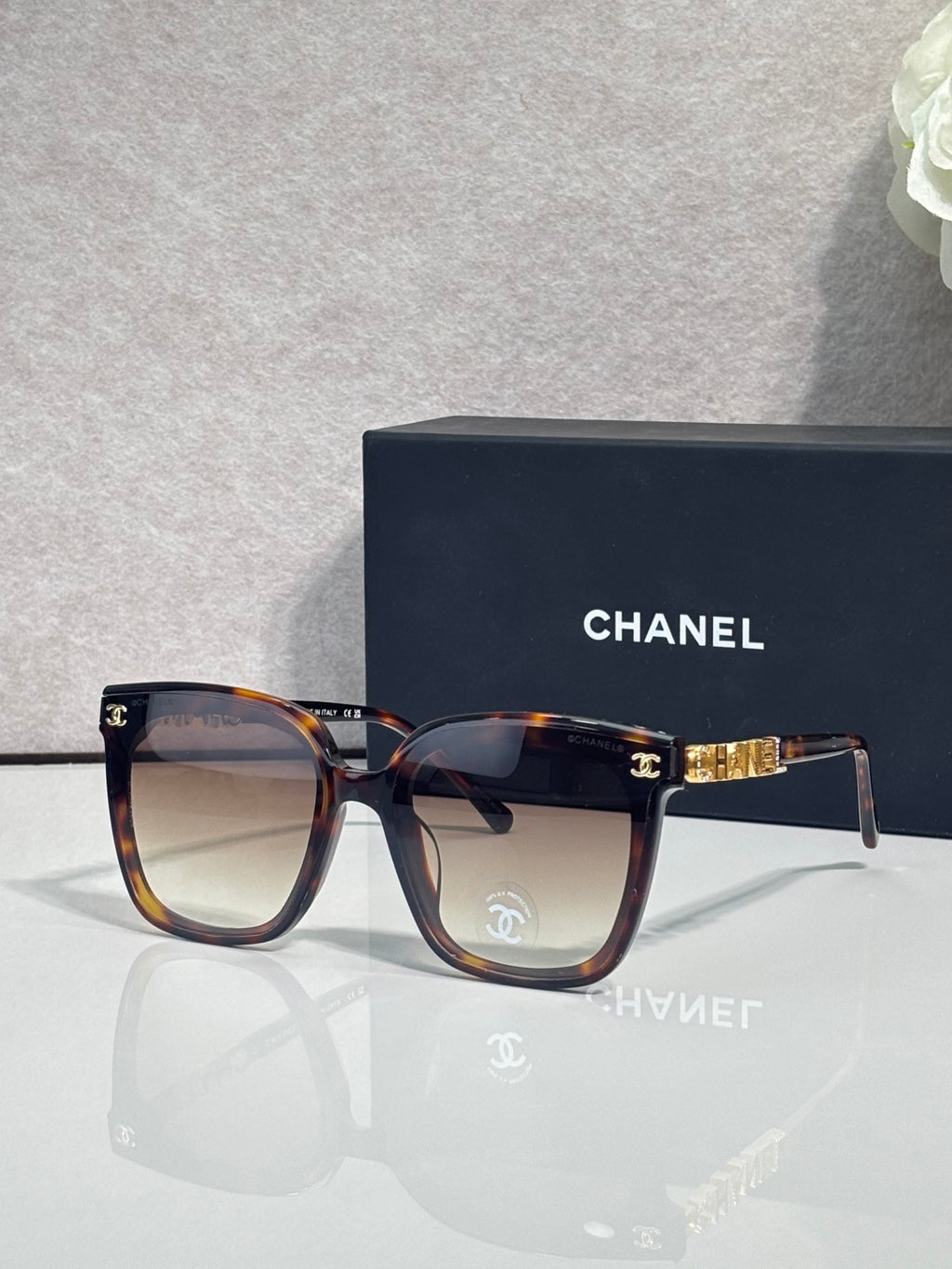 Square sunglasses with tortoiseshell frames and dark gray lenses, gold logo accent on temple