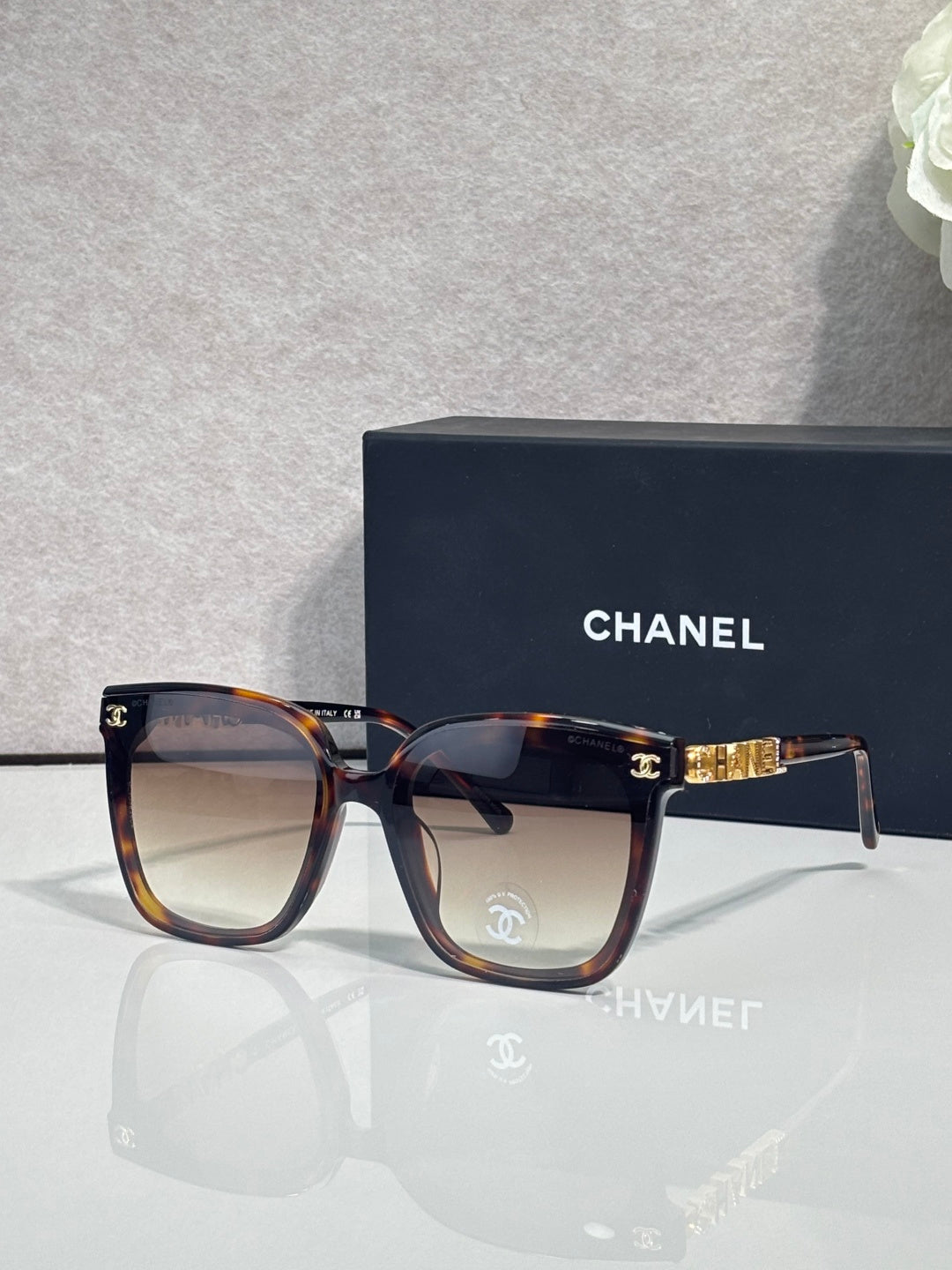 Square sunglasses with tortoiseshell frames and dark gray lenses, gold logo accent on temple