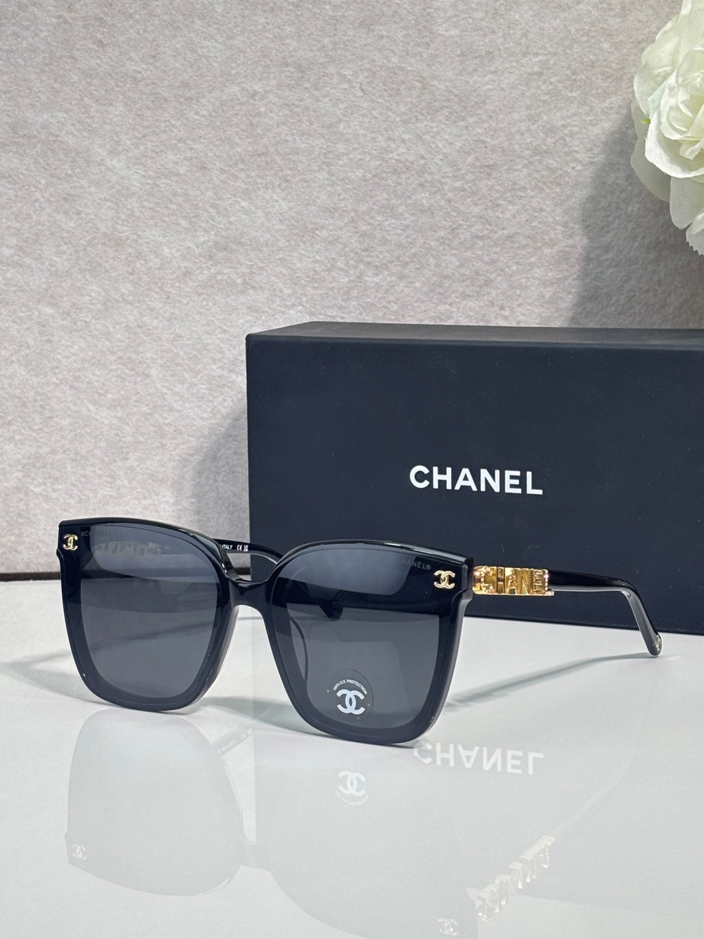 Square sunglasses with dark navy frames and dark gray lenses, gold logo on temple