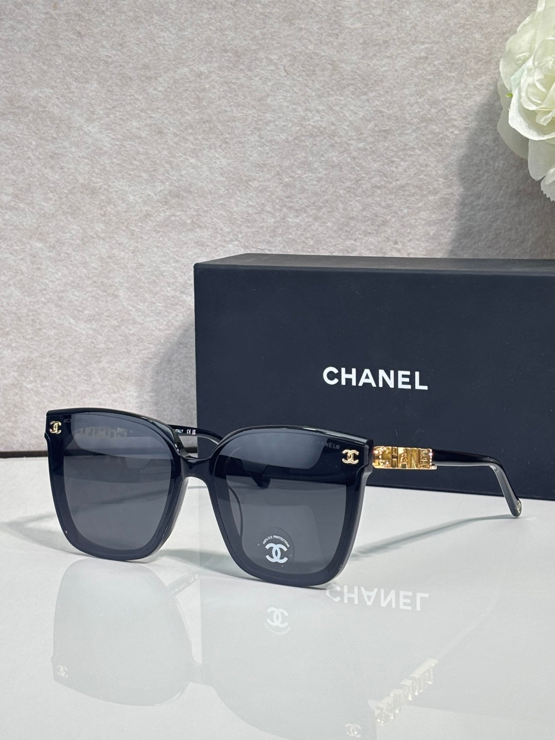 Square sunglasses with dark navy frames and dark gray lenses, gold logo on temple
