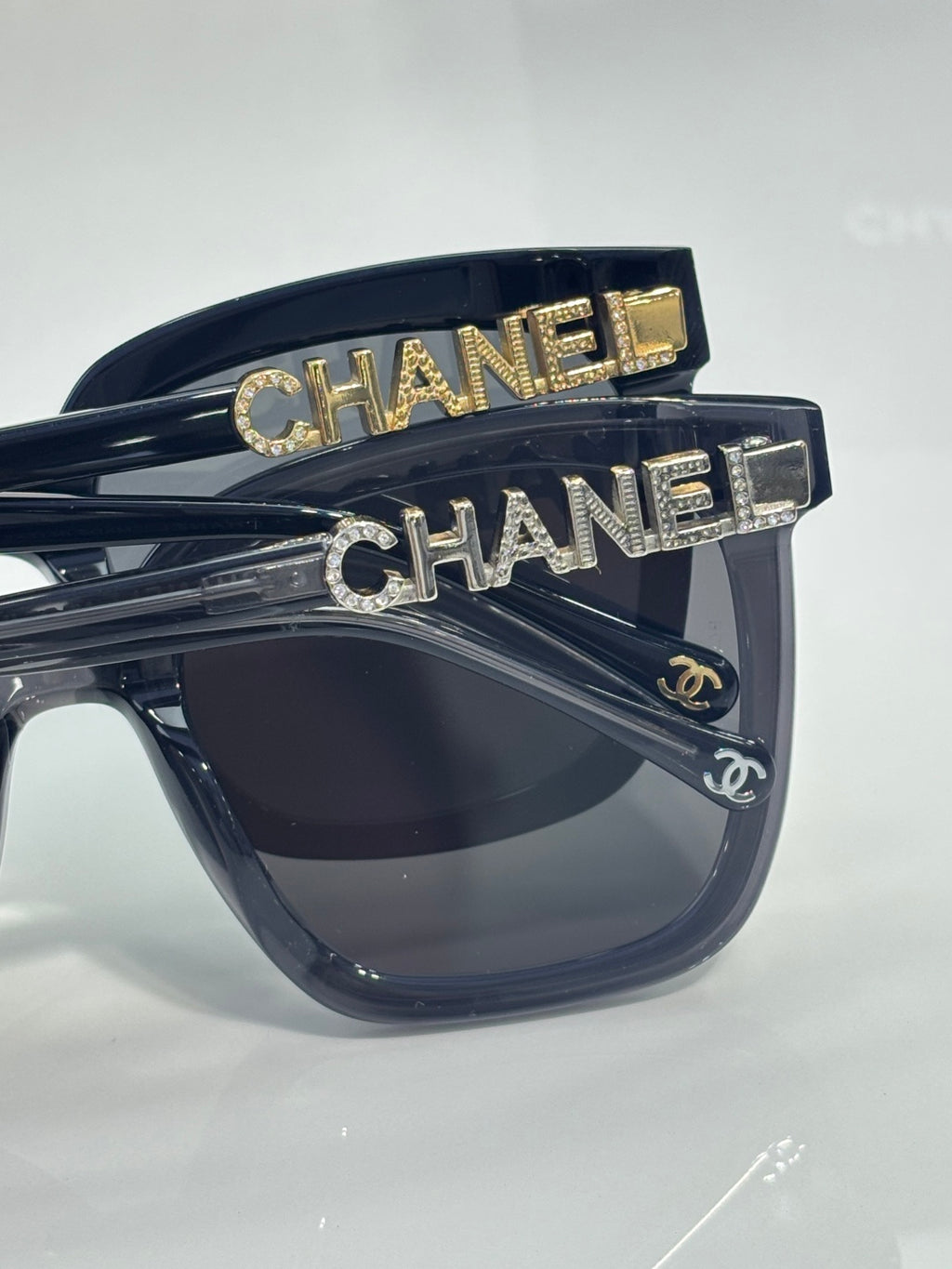 Cat-eye sunglasses with black frames and dark lenses, gold “CHANEL” lettering on temples