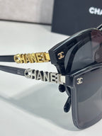 Sunglasses with dark frames, oversized lenses, and gold “CHANEL” logo on temple