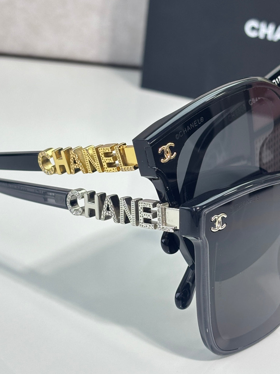 Sunglasses with dark frames, oversized lenses, and gold “CHANEL” logo on temple