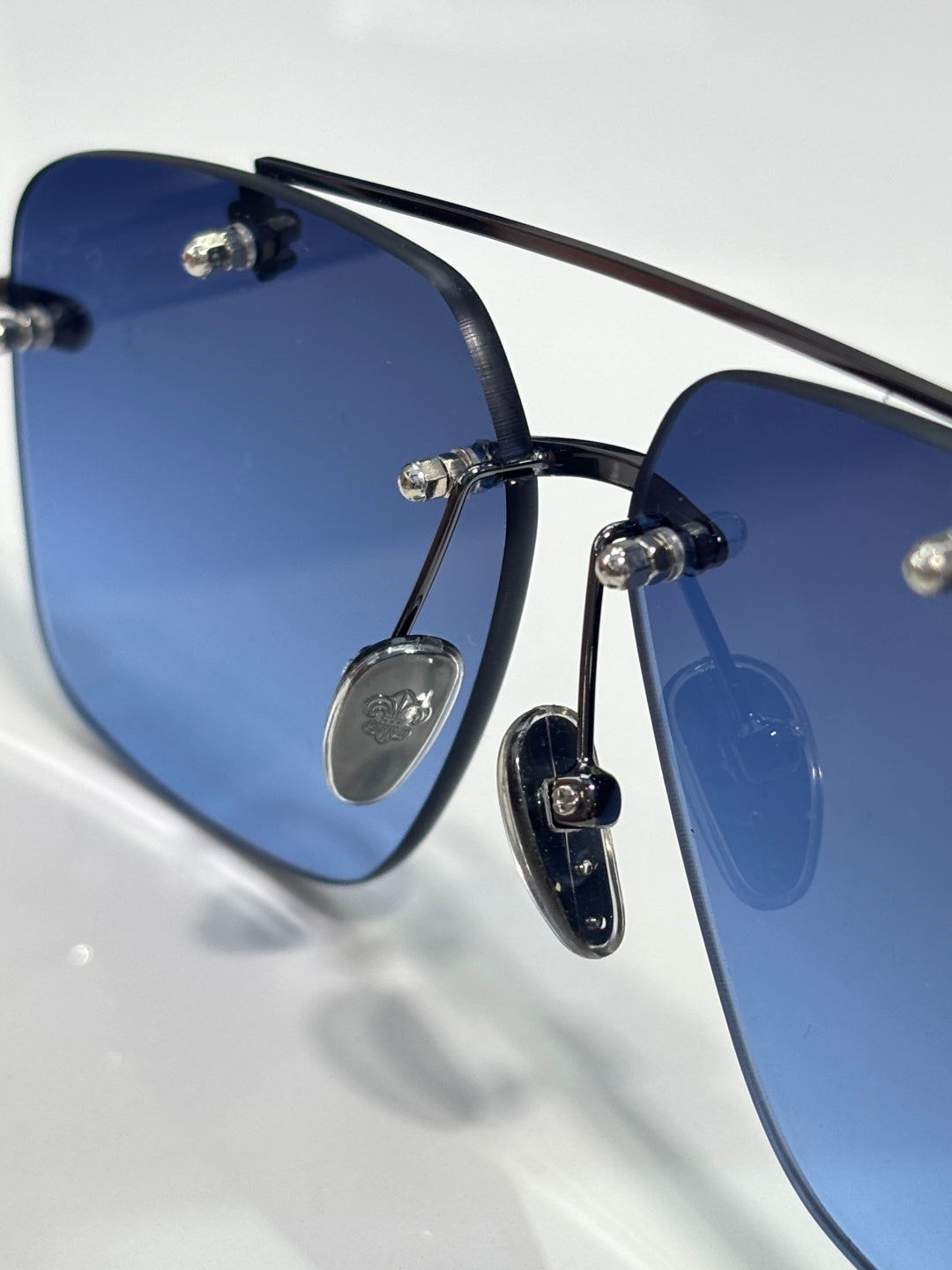 Close-up of chrome sunglasses showing dark blue lenses and black frame with gold-tone detail.