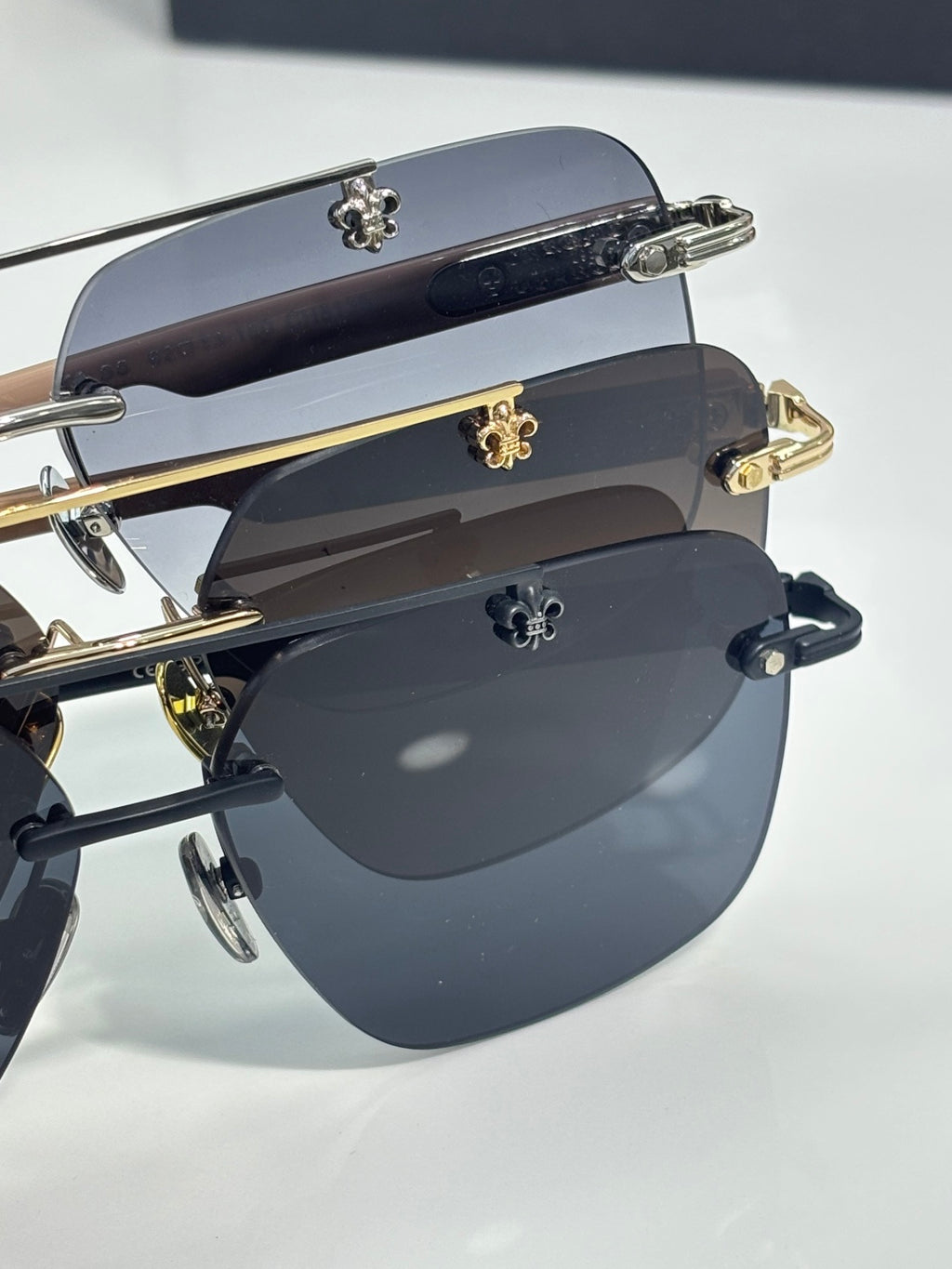 Stacked chrome sunglasses with dark blue lenses, metal frames, and gold-tone hinge embellishments.