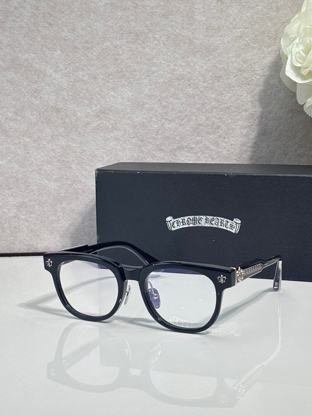 Navy blue full-rim glasses with clear lenses and gold-tone fleur-de-lis hardware