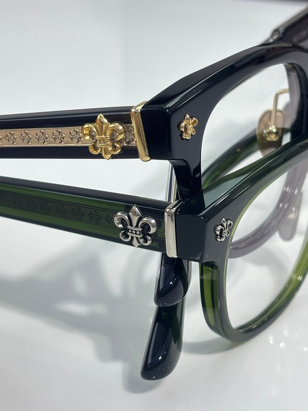 Dark blue glasses with green inner accents, gold fleur-de-lis temple hardware