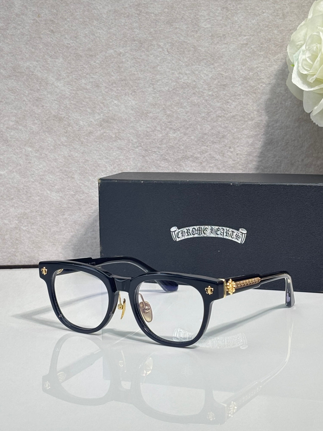 Black full-rim glasses with clear lenses and gold-tone decorative temple tips
