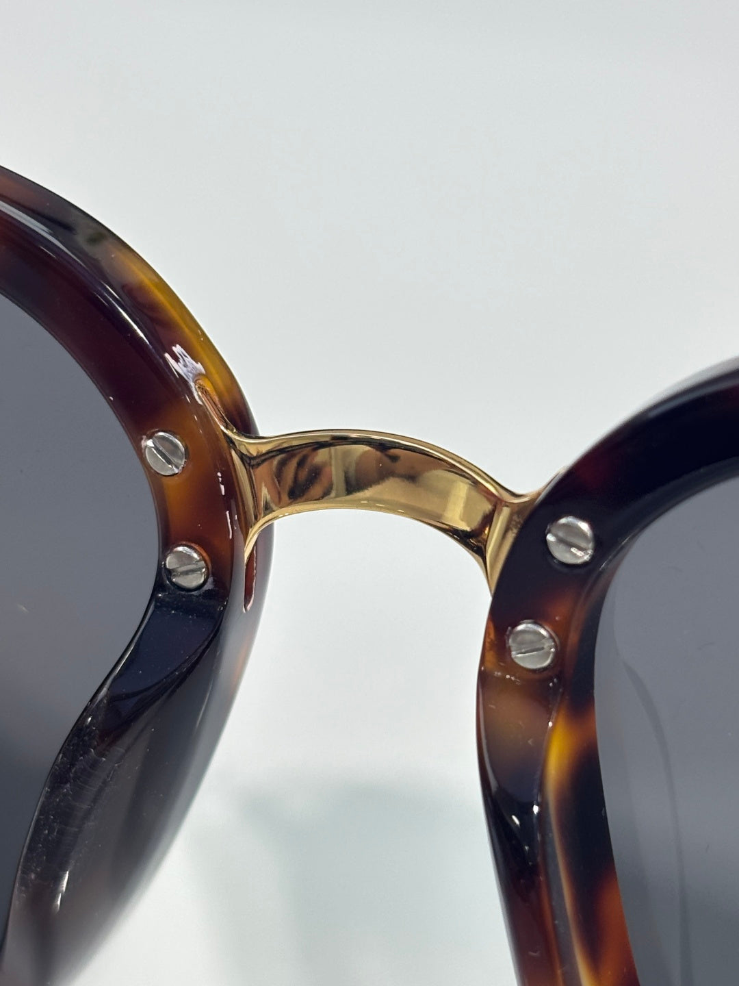 Chanel sunglasses close-up of tortoiseshell front with gold metal rivets and dark lens