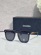 Chanel sunglasses with dark frames, dark lenses, and gold logo temple accents