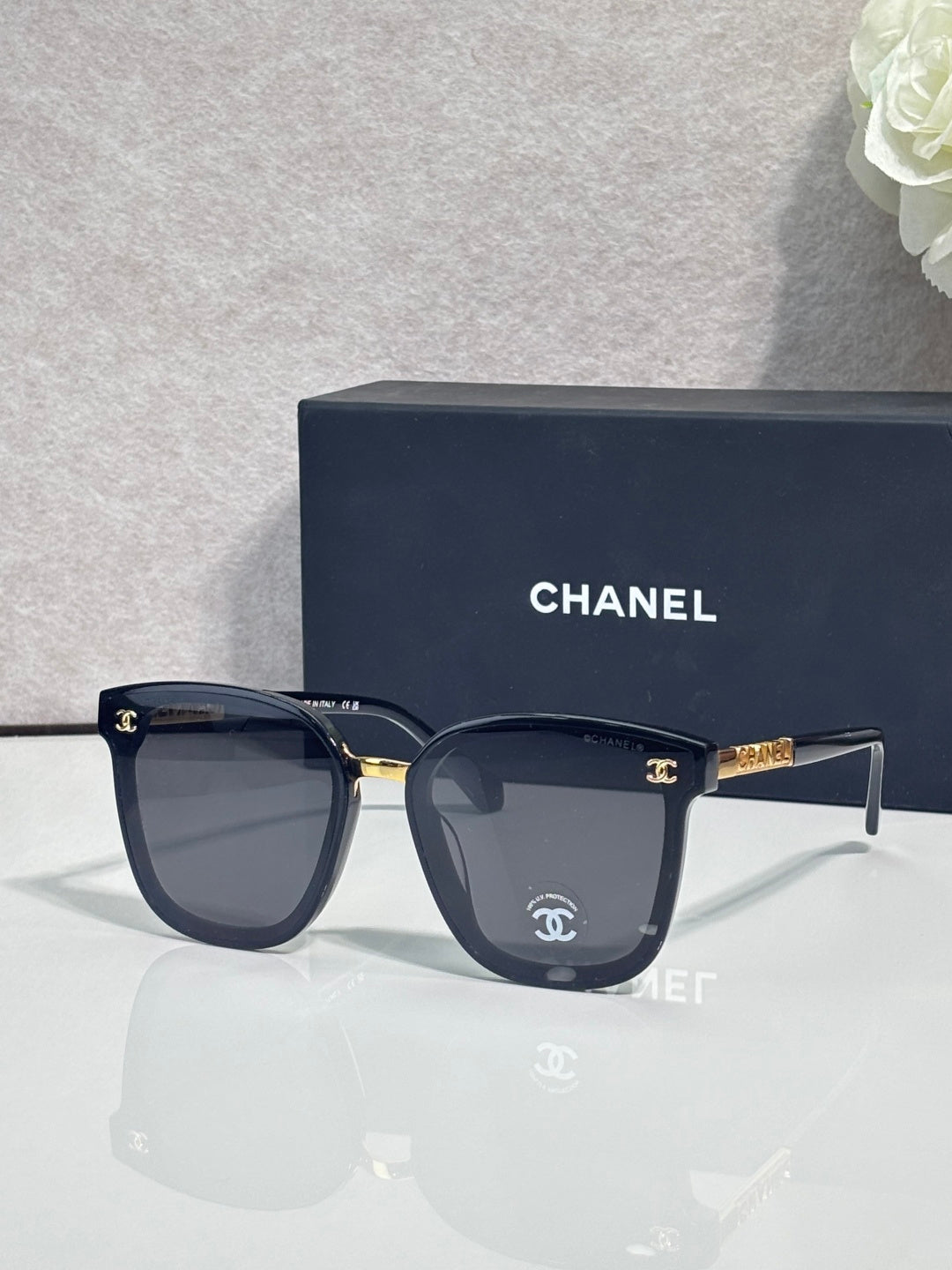 Chanel sunglasses with dark frames, dark lenses, and gold logo temple accents