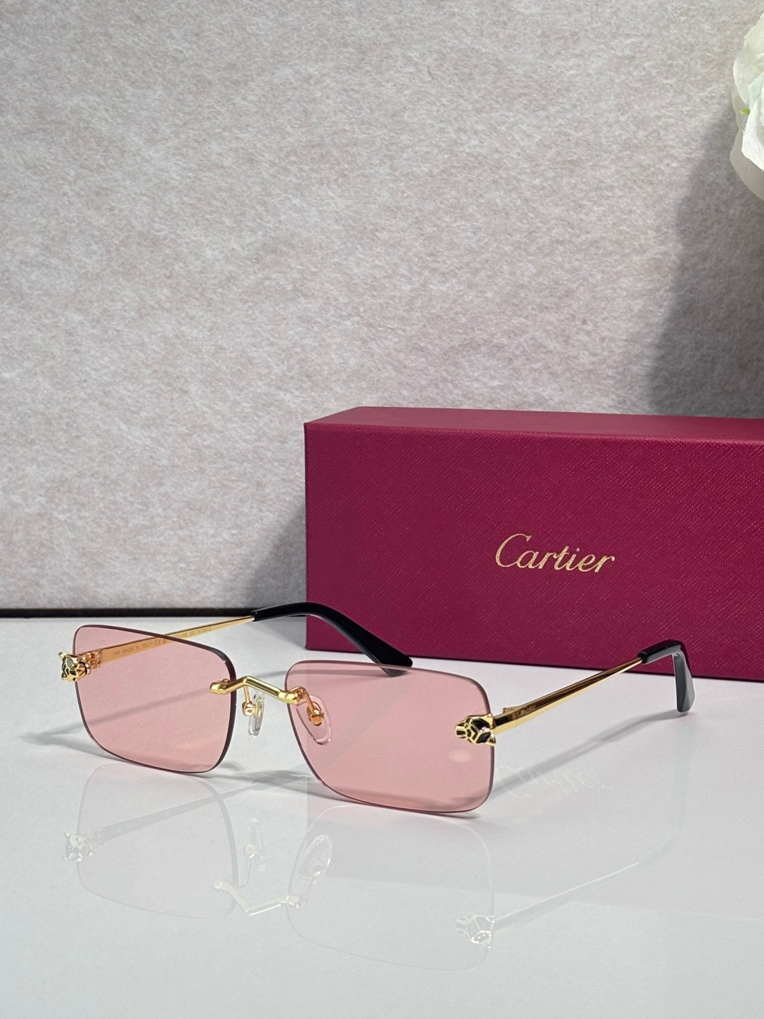 Rectangular eyeglasses with gold frame, light pink lenses, and black temple arms