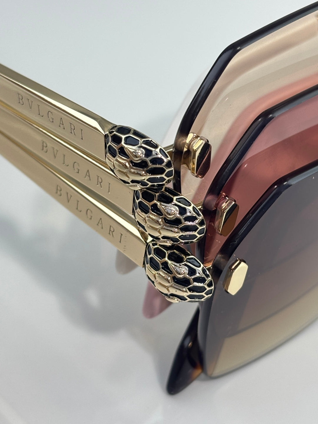 Close-up of gold-toned logo temples and black sunglasses frame with patterned hinge