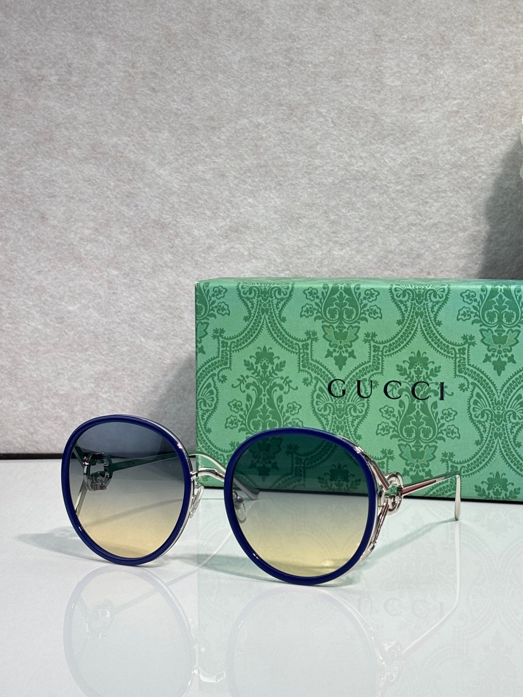 Round sunglasses with dark lenses; blue outer rims and gold-tone temples.