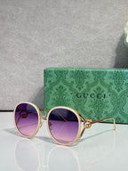 Round sunglasses with purple-tinted lenses; gold-tone frame and purple outer rims.