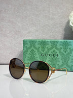 Round sunglasses with dark lenses and gold-tone frame; maroon outer rims.