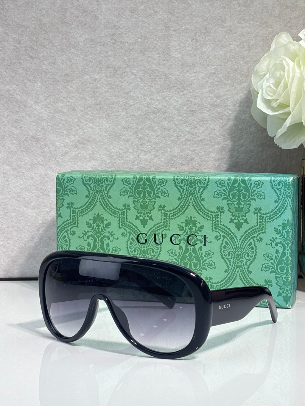 Gucci oversized sunglasses with dark frame and tinted lenses, placed in green logo case